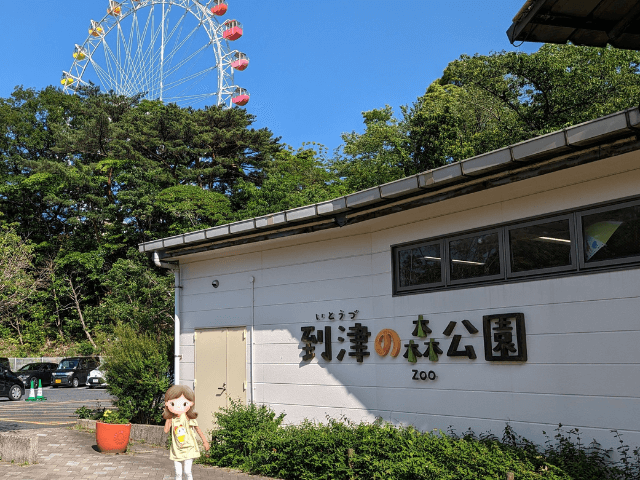 福岡県北九州市にある到津の森公園の「北ゲート」入口でカメラにピースしている女の子の画像。バックには園内の観覧車がある。